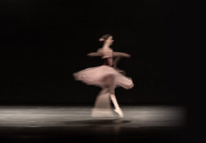 Ballet dancer in a pink tutu spinning on stage with blurred motion against a dark background, mid-dance.