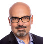 Professional headshot of a bald man with glasses, wearing a dark blazer and light blue shirt, looking at the camera.